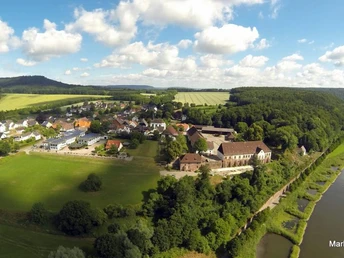 Weserhöhen_Weserpartie_Blankenau Luftaufnahme eines Dorfes mit umliegenden Feldern, Wälder und einem Flussufer im Sonnenschein.