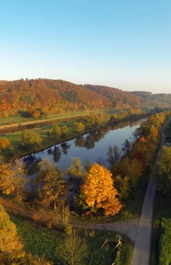 Weserhöhen_Weserradweg_Wehrden Herbstliche Luftaufnahme des Weserradwegs bei Wehrden, eingerahmt von einem von Laubbäumen gesäumten Fluss.