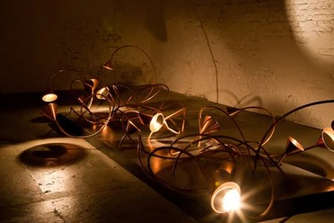 Lindenbrauerei Moderne Kunstinstallation mit verschlungenen Metallröhren und integrierten Lichtquellen im dunklen Raum.