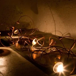 Lindenbrauerei Moderne Kunstinstallation mit verschlungenen Metallröhren und integrierten Lichtquellen im dunklen Raum.