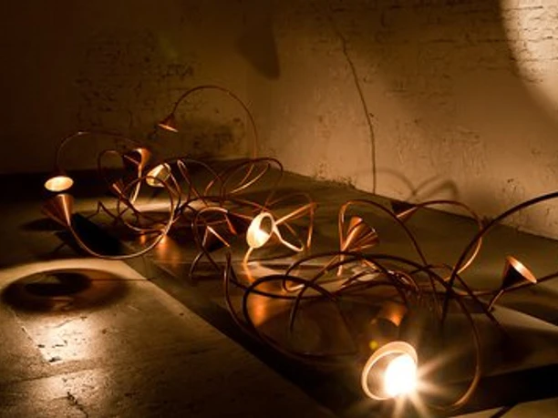 Lindenbrauerei Moderne Kunstinstallation mit verschlungenen Metallröhren und integrierten Lichtquellen im dunklen Raum.