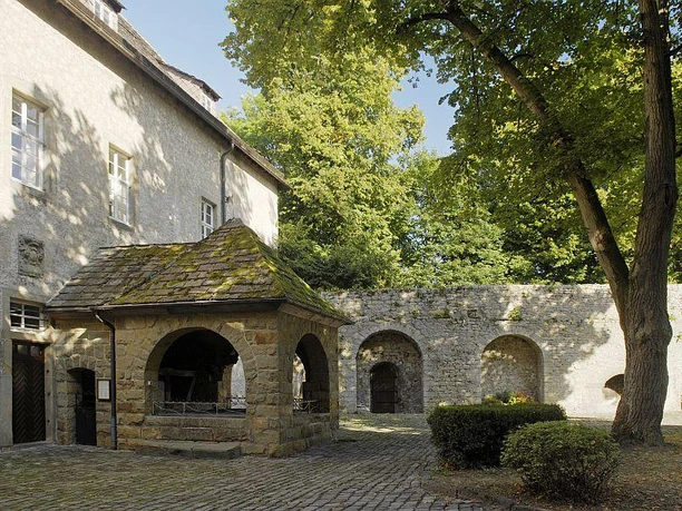 Burg Dringenberg - Innenhof Innenhof der Burg Dringenberg mit historischem Brunnen, von alten Mauern und schattigen Bäumen umgeben.