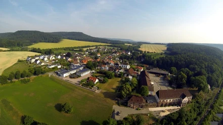 Blankenau rechts Hegge links Bierenberg mitte Wildberg Luftaufnahme eines Dorfes, umgeben von Feldern und Wäldern, mit einer hügeligen Landschaft im Hintergrund.
