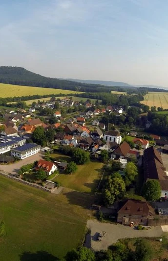 Blankenau rechts Hegge links Bierenberg mitte Wildberg Luftaufnahme eines Dorfes, umgeben von Feldern und Wäldern, mit einer hügeligen Landschaft im Hintergrund.