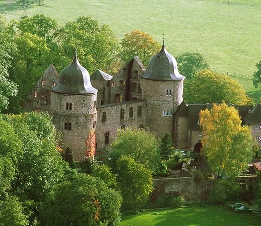 Die Sababurg liegt eingebettet in üppiges Grün und zeigt eine imposante Burganlage mit Türmen.
