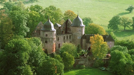 Sababurg Die Sababurg liegt eingebettet in üppiges Grün und zeigt eine imposante Burganlage mit Türmen.