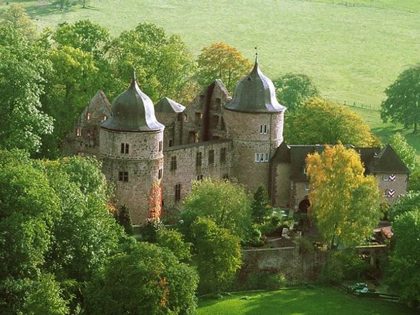 Sababurg Die Sababurg liegt eingebettet in üppiges Grün und zeigt eine imposante Burganlage mit Türmen.