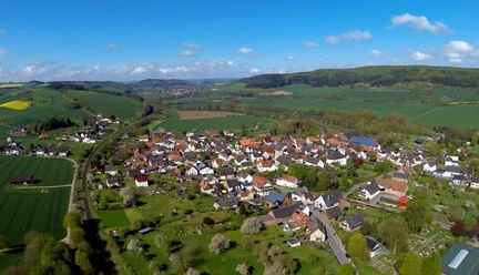 Blick auf Amelunxen Luftaufnahme von Amelunxen mit grünen Wiesen, Feldern und Hügeln unter einem klaren blauen Himmel.