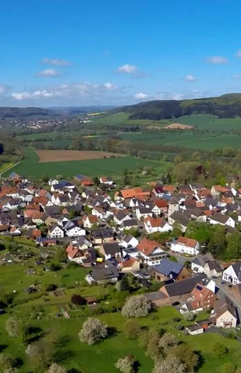 Blick auf Amelunxen Luftaufnahme von Amelunxen mit grünen Wiesen, Feldern und Hügeln unter einem klaren blauen Himmel.
