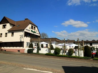 Einkehr in Blankenau Gasthaus an einer Straße, mit Sonnenterrasse und Gästen unter Schirmen, umgeben von Pflanzen.