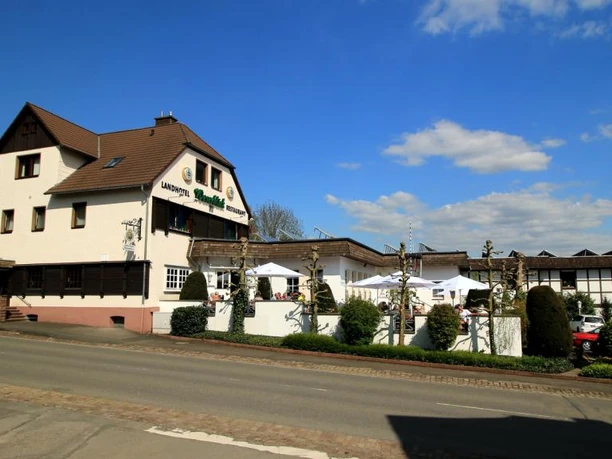 Einkehr in Blankenau Gasthaus an einer Straße, mit Sonnenterrasse und Gästen unter Schirmen, umgeben von Pflanzen.