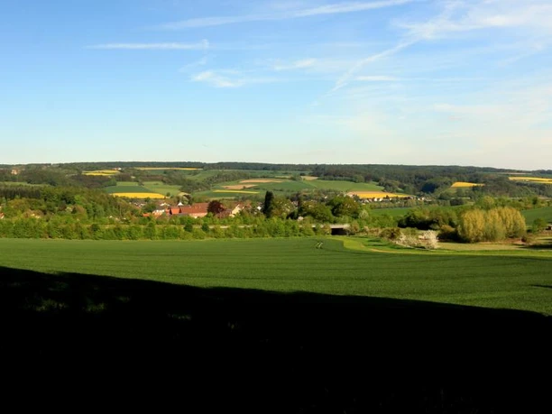 Blick auf Blankenau Sanfte Hügel mit Feldern und Bäumen, vereinzelte Gebäude und ein weitläufiger blauer Himmel.