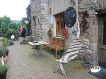 Krusfelder Kaffeestube, die Einkehr lohnt immer. Eine rustikale Steinfassade mit Holzbank, Gartentisch und Wanddekoration unter freiem Himmel.