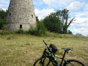 Aussichtsturm Eilenberg oberhalb von Barntrup Runder Steinturm auf einer Wiese, im Vordergrund ein abgestelltes grünes Fahrrad, blauer Himmel.
