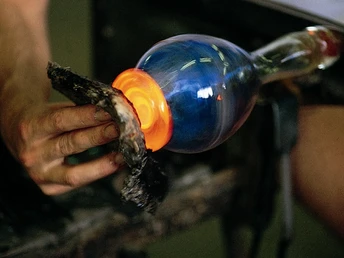 Glasbläser in der ehemaligen Glasbläserei Ein Glasbläser formt mithilfe von Werkzeugen und Hitze eine leuchtende Glasstruktur.