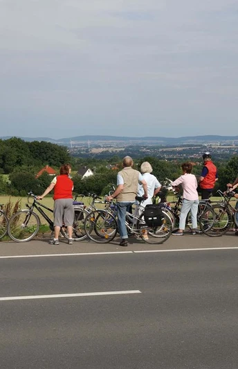 Eine Radlergruppe genießt die Weitsicht über grüne Hügel und Felder des Ravensberger Hügellands.