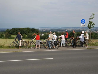 Blick auf das Ravensberger Hügelland Eine Radlergruppe genießt die Weitsicht über grüne Hügel und Felder des Ravensberger Hügellands.