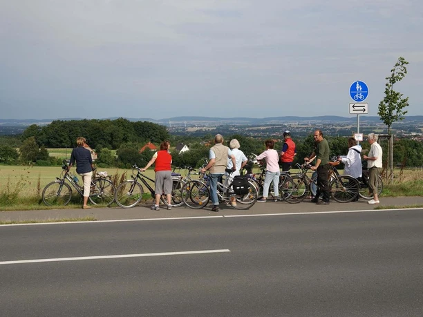 Blick auf das Ravensberger Hügelland Eine Radlergruppe genießt die Weitsicht über grüne Hügel und Felder des Ravensberger Hügellands.