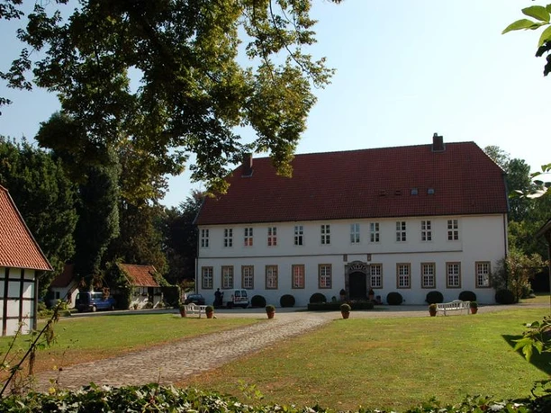 Gut Hiddenhausen Historischer Gutshof mit rotem Dach, flankiert von Fachwerkgebäuden, umgeben von grüner Natur.