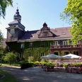 Schloss Mühlenburg mit Efeu bewachsen, Turm mit Uhr, Terrasse mit Tischen und Sonnenschirmen.