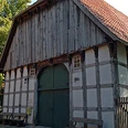 Historisches Fachwerkhaus mit großem Holztor und Ziegeldach, umgeben von Bäumen.