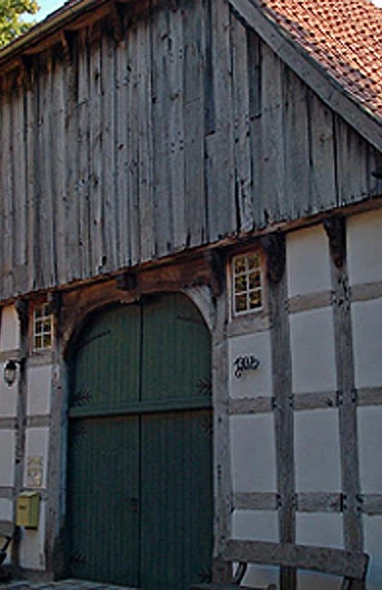 Historisches Fachwerkhaus mit großem Holztor und Ziegeldach, umgeben von Bäumen.