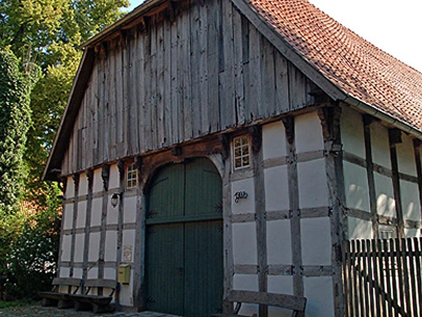 Holzhandwerksmuseum Hiddenhausen Historisches Fachwerkhaus mit großem Holztor und Ziegeldach, umgeben von Bäumen.