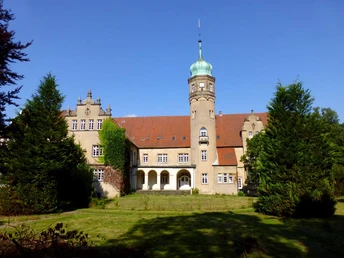 Historisches Wasserschloss mit markantem Turm, umgeben von gepflegtem Rasen und hohen Bäumen.