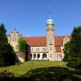 Wasserschloss Ulenburg Historisches Wasserschloss mit markantem Turm, umgeben von gepflegtem Rasen und hohen Bäumen.