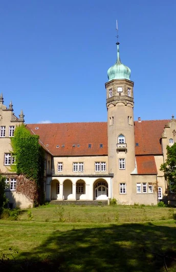 Wasserschloss Ulenburg Historisches Wasserschloss mit markantem Turm, umgeben von gepflegtem Rasen und hohen Bäumen.