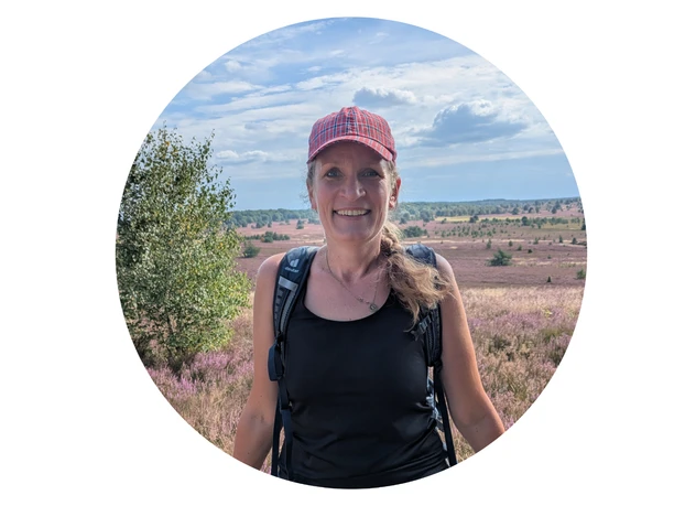 Wanderführerin Marthe Kniep mit roter Kappe vor blühender Heidelandschaft.