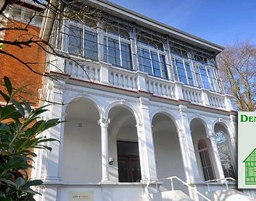 Ein historisches Gebäude mit weißen Säulen und großer Fensterfront in urbaner Umgebung.