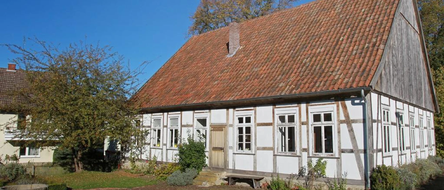 Museumsschule Hiddenhausen Ein historisches Fachwerkgebäude mit blumengeschmücktem Garten und roten Dachziegeln bei Sonnenlicht.