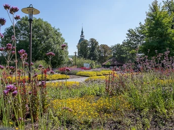 Flora-Westfalica-Park Blumenreiche Parkanlage mit verschlungenen Wegen, im Hintergrund ein Kirchturm, umgeben von Bäumen.