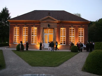 Orangerie Rotes Backsteingebäude mit großer Fensterfront, abends beleuchtet, Besucher im Vordergrund.