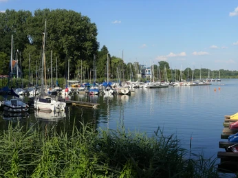 Segelboote am Steg Segelboote liegen vertäut an einem Steg eines ruhigen Sees, im Hintergrund sind Bäume sichtbar.