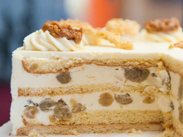 Torte essen im Landhaus Blumengarten Eine aufgeschnittene Sahnetorte mit hellem Biskuit und weißen Cremefüllungen, verziert mit Krokant.