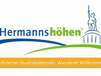 Qualitätsbetrieb der Hermannshöhen Zertifikat-Logo der Hermannshöhen mit "Wanderer Willkommen" und Denkmal-Symbol im Hintergrund.
