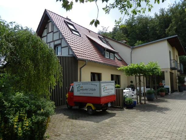Außenansicht, Landgasthof Mücke in Marsberg Ein zweigeschossiger Landgasthof mit rotem Satteldach und Fachwerkelementen, umgeben von Bäumen.