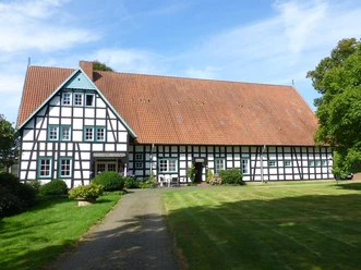 Hof Oberwahrenbrock Fachwerkhaus auf gepflegtem Rasen, Hof Oberwahrenbrock, mit großen Dach und weiß-schwarzen Strukturen.