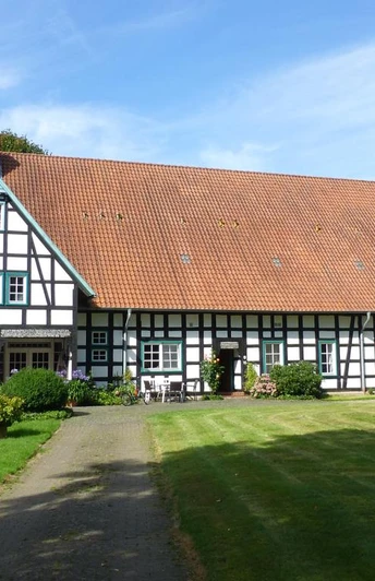 Hof Oberwahrenbrock Fachwerkhaus auf gepflegtem Rasen, Hof Oberwahrenbrock, mit großen Dach und weiß-schwarzen Strukturen.