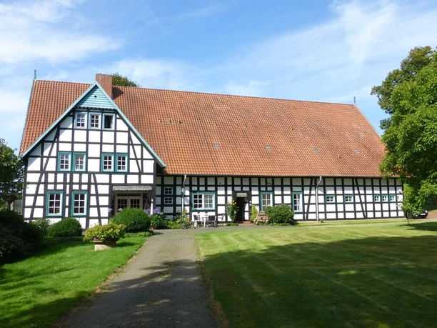 Hof Oberwahrenbrock Fachwerkhaus auf gepflegtem Rasen, Hof Oberwahrenbrock, mit großen Dach und weiß-schwarzen Strukturen.