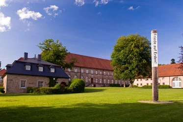 Historische Gebäude mit roten Ziegeldächern und grüne Wiese, blauer Himmel, Friedenspfahl.