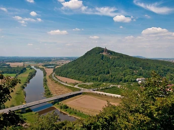 Blick auf die Porta Westfalica mit Fluss, bewaldetem Berg und Kaiser-Wilhelm-Denkmal an sonnigem Tag.