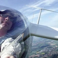 Person in einem Segelflugzeug, fotografiert aus der Pilotenkabine, überblickt Felder und Landschaften.