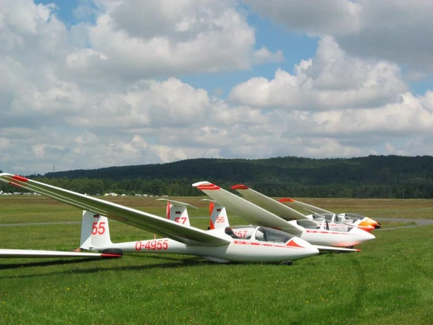 Segelflieger auf Flugplatz Oerlinghausen Mehrere Segelflugzeuge auf einer Wiese am Flugplatz Oerlinghausen unter wolkigem Himmel.