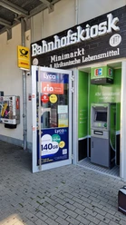 Eingang zum Bahnhofskiosk mit Geldautomat, Post- und DHL-Schild sowie Mobilfunkwerbung