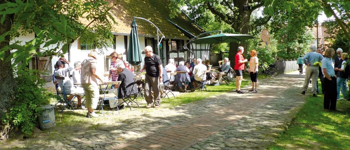 Haus Windheim No2 mit Hofecafé Ein lebendiges Café im Innenhof, umgeben von grünen Bäumen, wo Menschen entspannt plaudern.