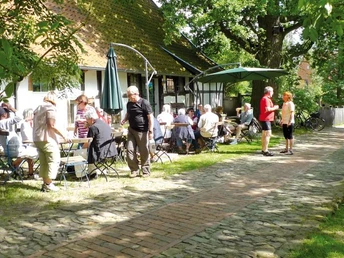 Haus Windheim No2 mit Hofecafé Ein lebendiges Café im Innenhof, umgeben von grünen Bäumen, wo Menschen entspannt plaudern.