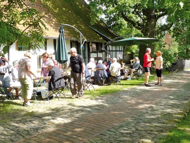 Haus Windheim No2 mit Hofecafé Ein lebendiges Café im Innenhof, umgeben von grünen Bäumen, wo Menschen entspannt plaudern.